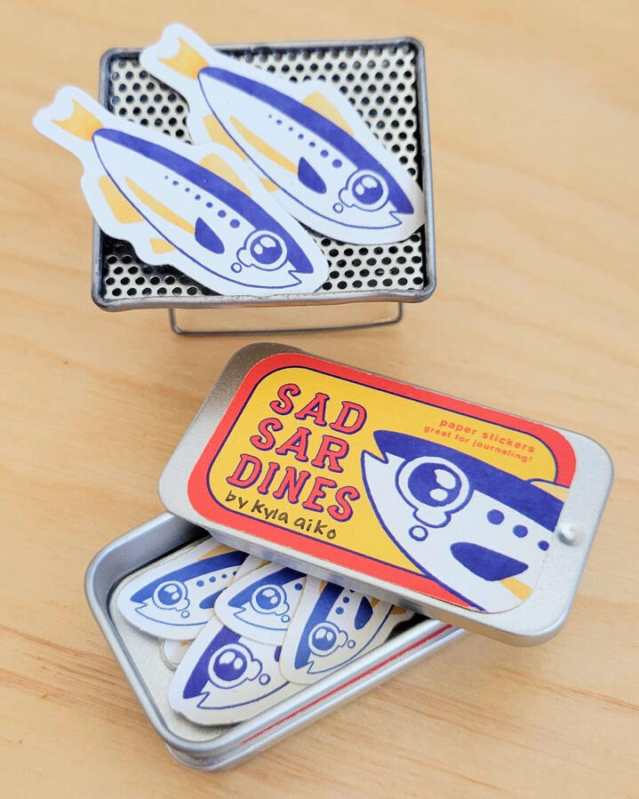 In-person comic festival setup. Sardine stickers are on mini BBQ grills // Photo credit: @msanchez.studio and @cacollegeofarts